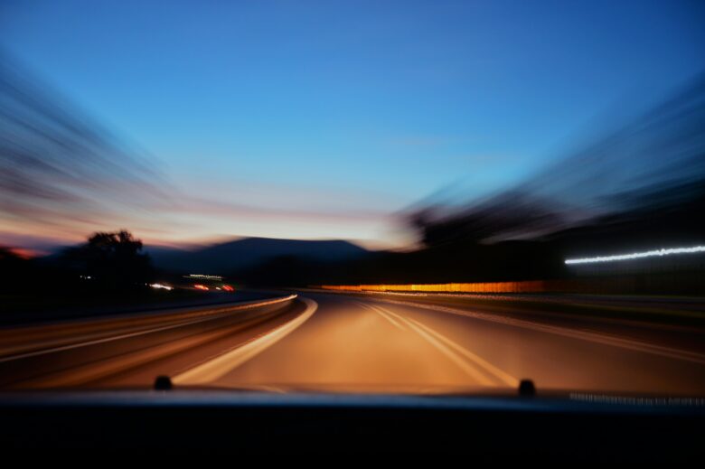Blurred perspective from a car on a road at dusk, illustrating the difficulty of reading signs while driving at speed."