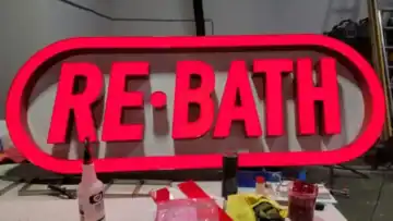 Red illuminated RE-BATH channel letters on a custom oval raceway during final fabrication in the workshop.