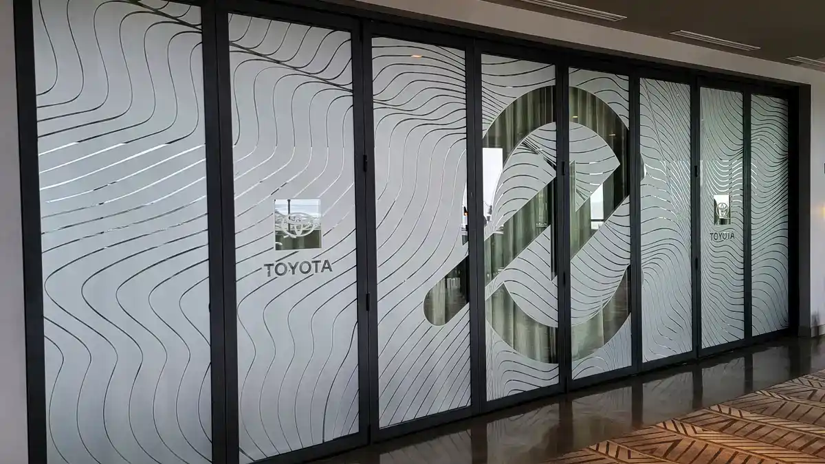 Custom frosted glass vinyl film installed on a wall of folding glass doors for a Toyota/Toyoda event in Encinitas, featuring a large abstract wave pattern and corporate logos.
