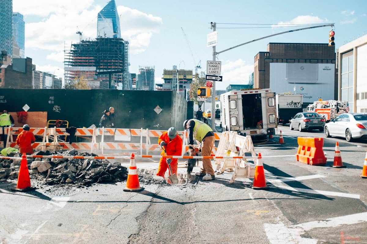 Construction workers repairing city street with safety cones and barriers.