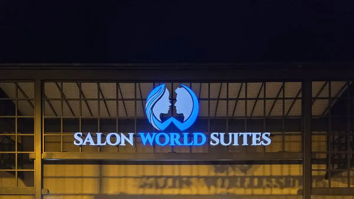 Illuminated Salon World Suites sign with logo at night.